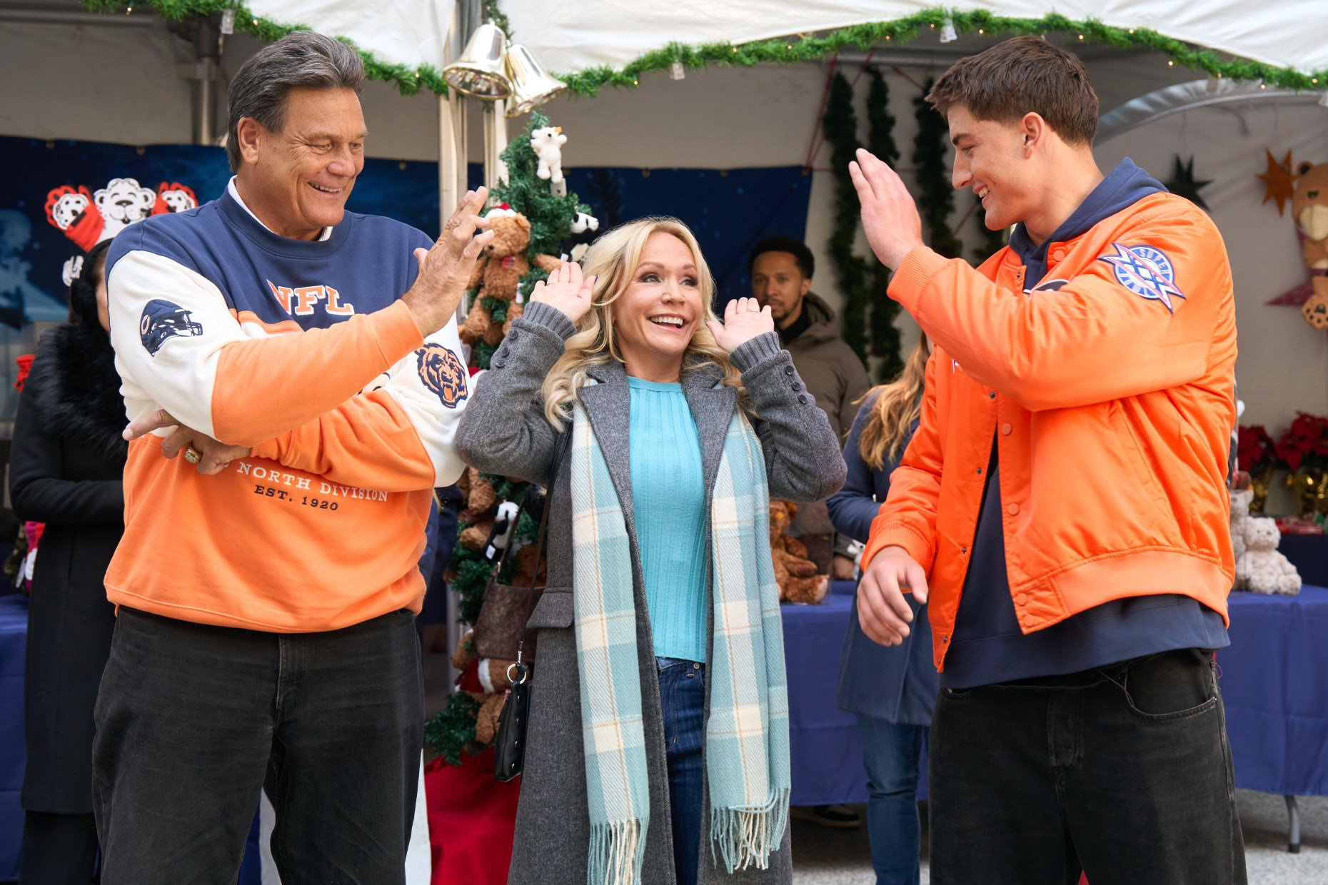 Former Bears player Dan Hampton, Jody (Barbara Alyn Woods) and tight end Colston Loveland high-five while watching a cornhole tournament in "Holiday Touchdown: A Bears Love Story." (Elizabeth Sisson/Hallmark Media)
