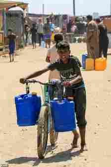 A boy pushes a bicycle loaded with two jerrycans after filling up from a water truck in Rafah in the southern Gaza Strip