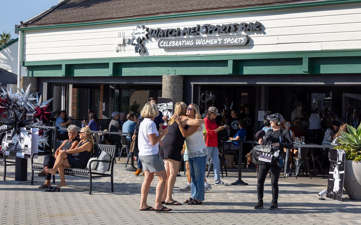 Patrons greet each other as they arrive at the bar, ordering food and drinks and watching women's sports during the grand opening of Watch Me! Sports Bar in Long Beach Friday, July 26, 2024