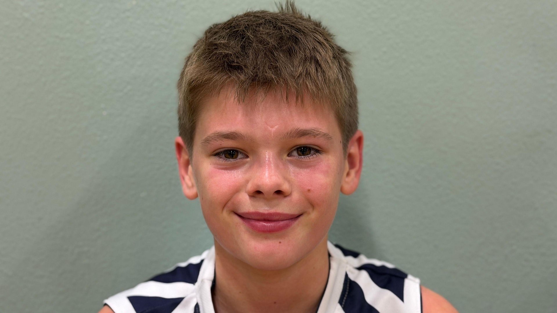 Photo of young basketball player against a green wall.