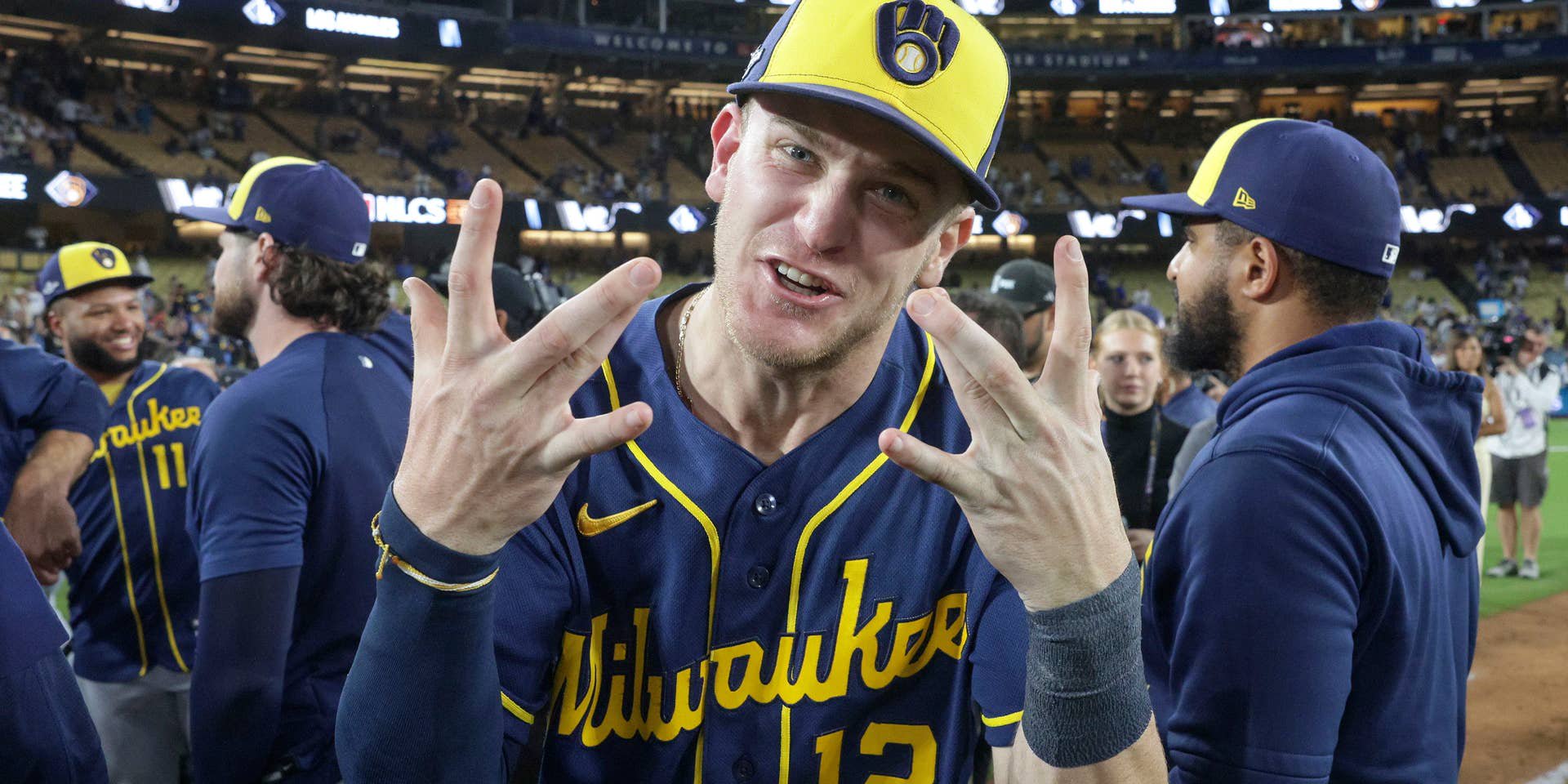 Ein Profi der Milwaukee Brewers feiert im blau-gelben Trikot und mit Baseballcap den Aufstieg ins MLB-Finale mit Jubelgesten vor seinen Teamkollegen auf dem Feld.