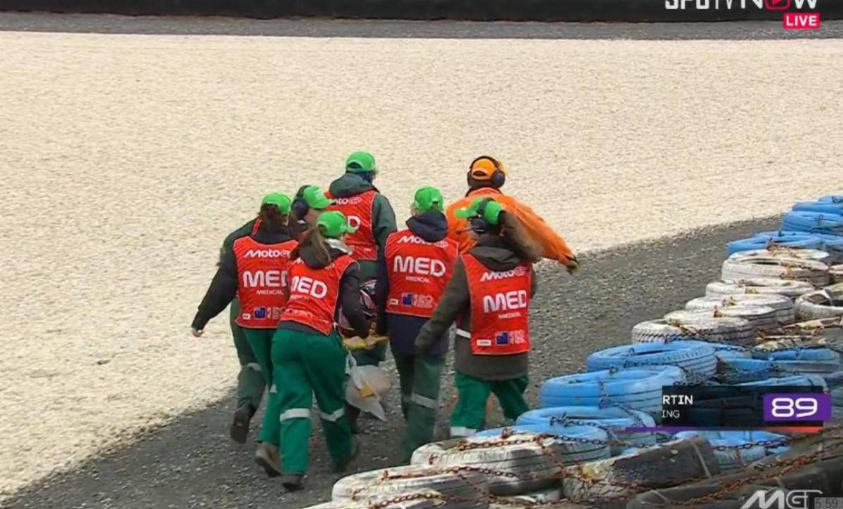 Medical marshals in green and orange bibs carry an injured rider across gravel toward a tyre wall after a crash at MotoGP's Australian GP