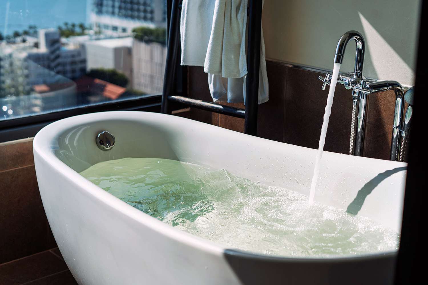Elegant bathroom setup featuring a modern bathtub filled with water, placed by a large window offering a breathtaking city view. 