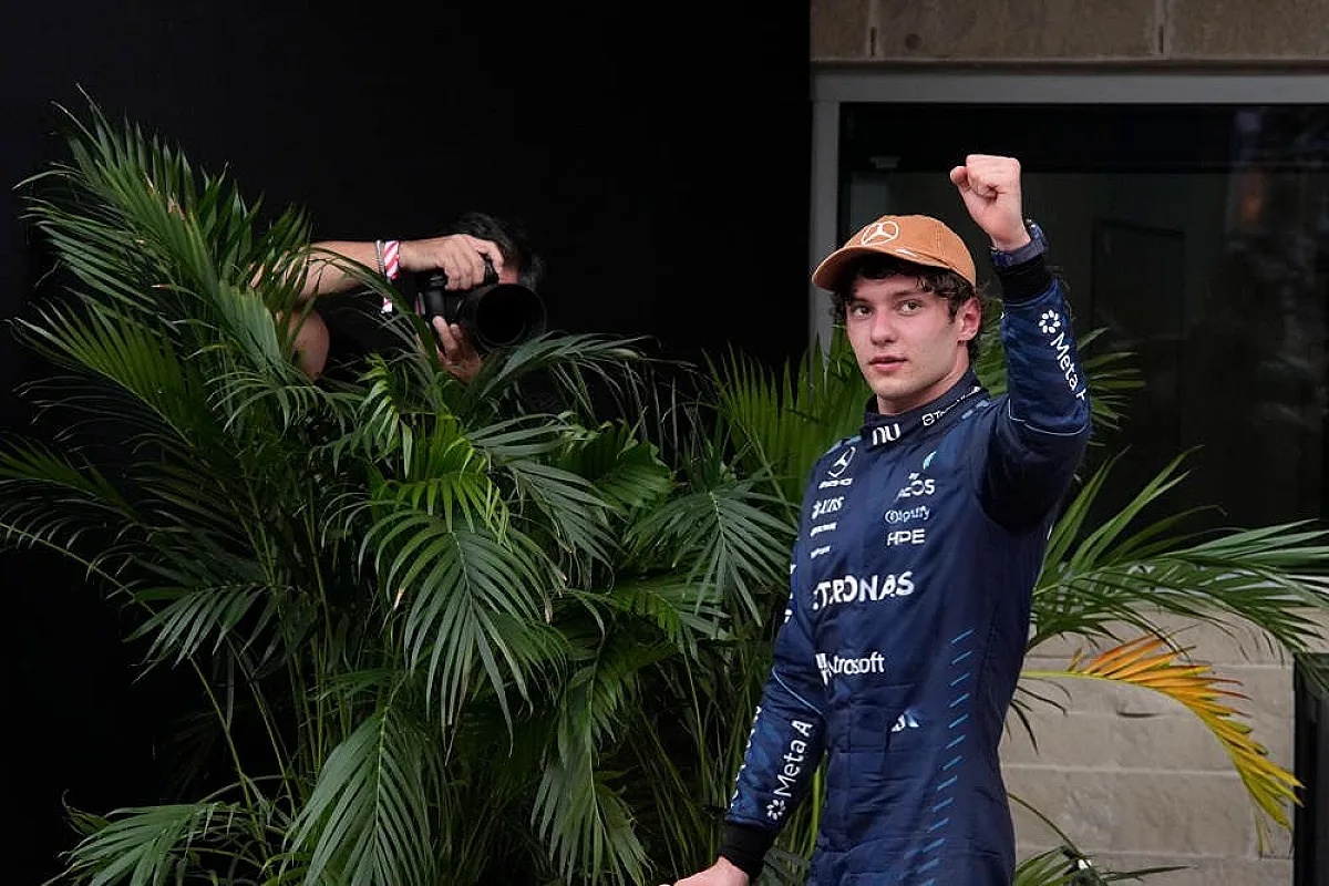 A Mercedes F1 driver in a navy race suit and tan cap raises a fist in celebration beside palm plants at the Mexico GP paddock