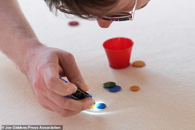 Umpire Harley Jones uses a torch to check whether 'winks' are touching during the 2026 World Singles Tiddlywinks Championship