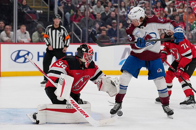 New Jersey Devils goaltender Jake Allen, left, defends the net while Colorado Avalanche's T.J. Hughes looks on during the third period of an NHL hockey game in Newark, N.J., Tuesday, Oct. 20, 2026. (AP Photo/Seth Wenig)