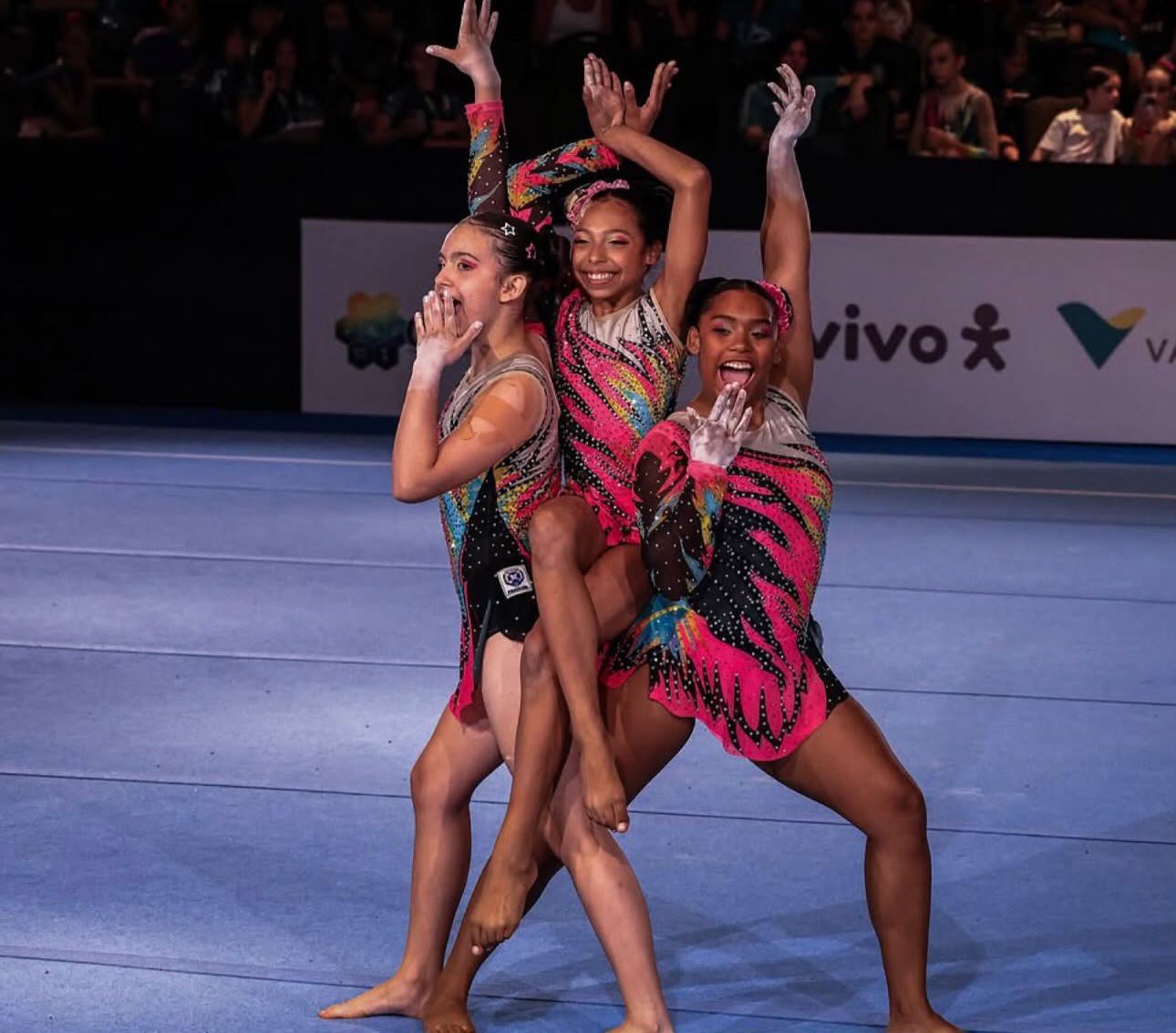 O trio formado por Sabrina de Andrade, Giovana Santin e Victória Olívio realiza uma pose acrobática expressiva durante a sua apresentação de ginástica.