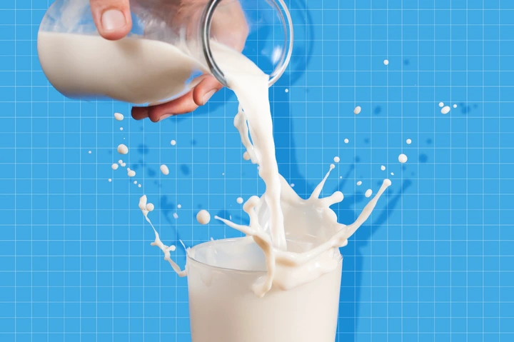 Milk from a jug pouring into glass on a blue background