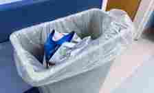 A trash can containing disposed blue and white medical items, located in a clinical or hospital setting