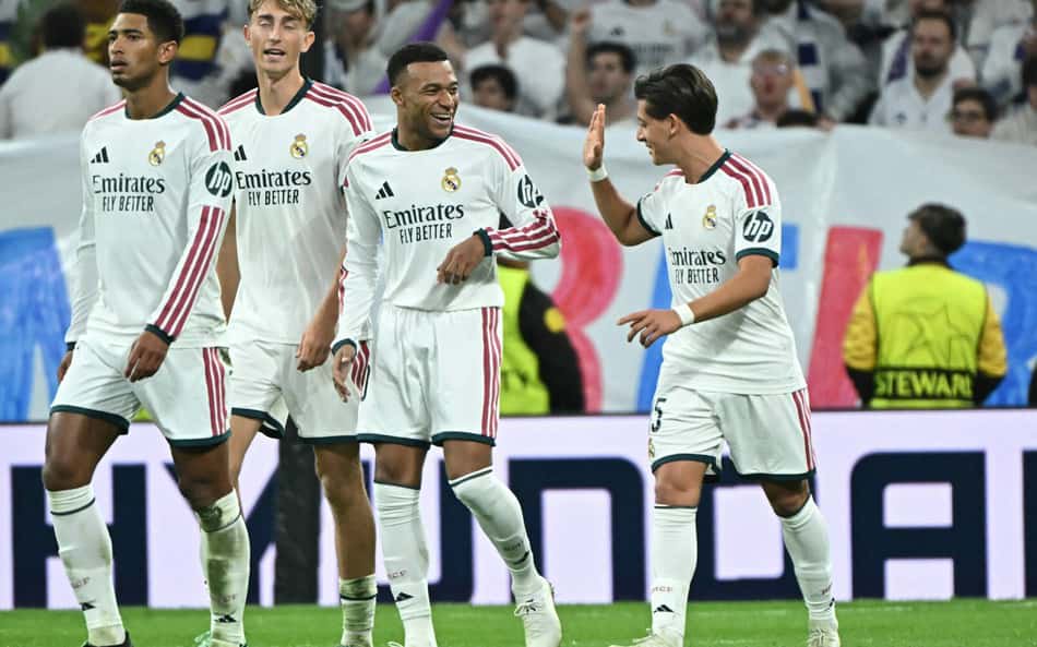 O meio-campista turco do Real Madrid, número 15, Arda Guler (à direita), gesticula para o atacante francês do Real Madrid, número 10, Kylian Mbappé, enquanto comemora o segundo gol de sua equipe durante a partida da 3ª rodada da Liga dos Campeões da UEFA entre Real Madrid CF e RB Leipzig, no estádio Santiago Bernabéu, em Madri, em 21 de outubro de 2026. (Foto: Javier Soriano / AFP)