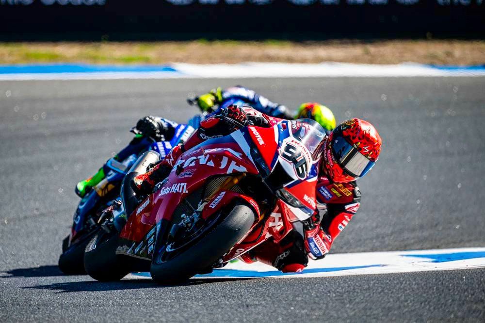 Rider in red and white Honda leathers and number 9 on his Honda superbike, leaning into a corner ahead of a rival in blue on a racetrack