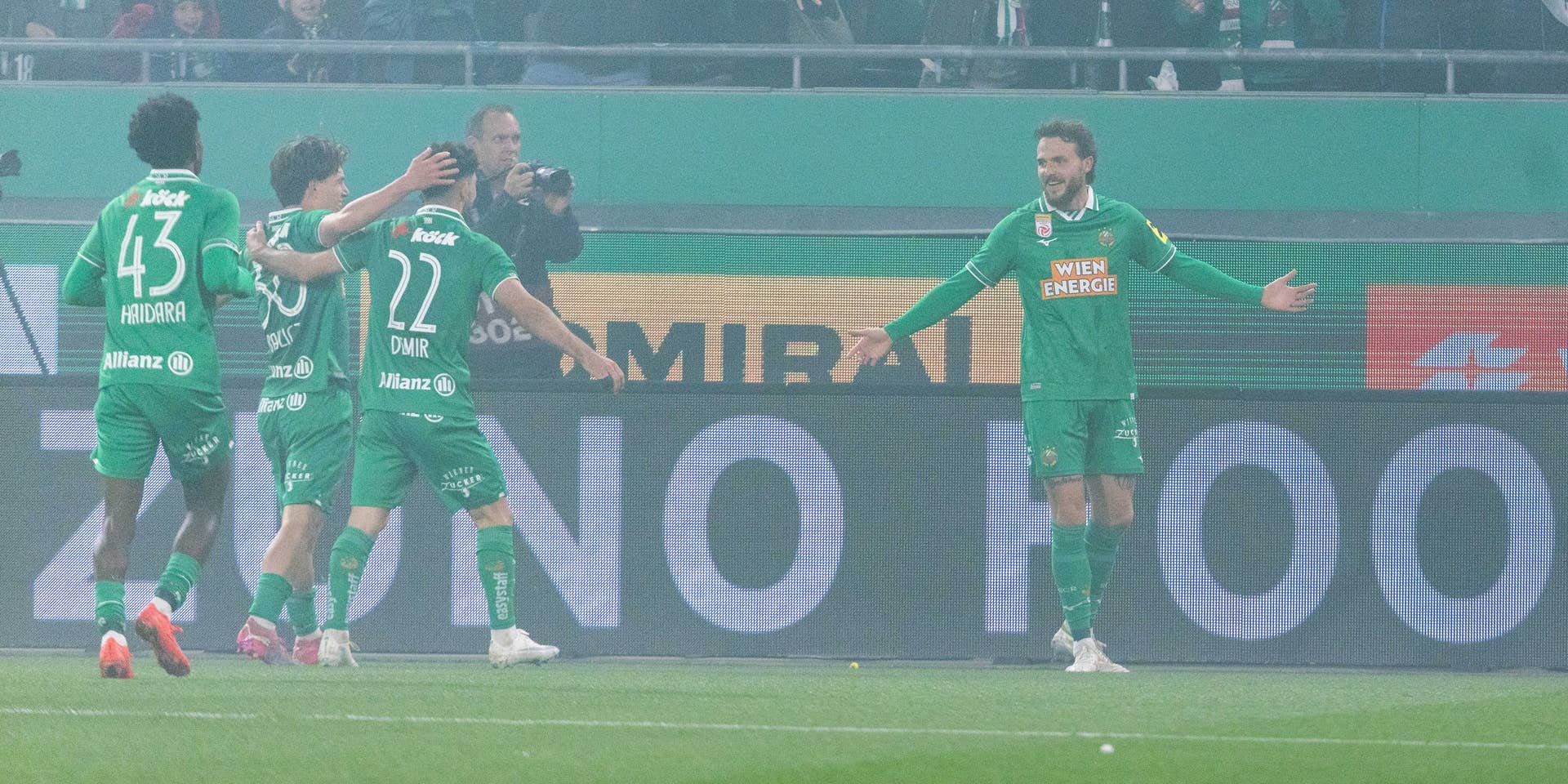 Jannes Horn läuft mit ausgebreiteten Armen im Nebel über den Rasen und feiert seinen Treffer gemeinsam mit seinen jubelnden Rapid-Teamkollegen.