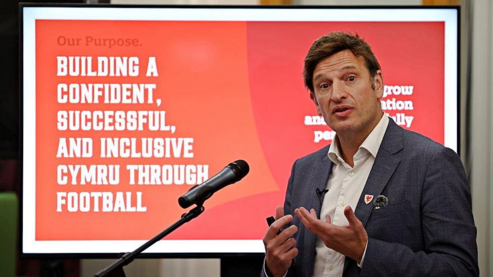 FAW CEO Noel Mooney making a speech in front of a microphone with a slide from a presentation behind him