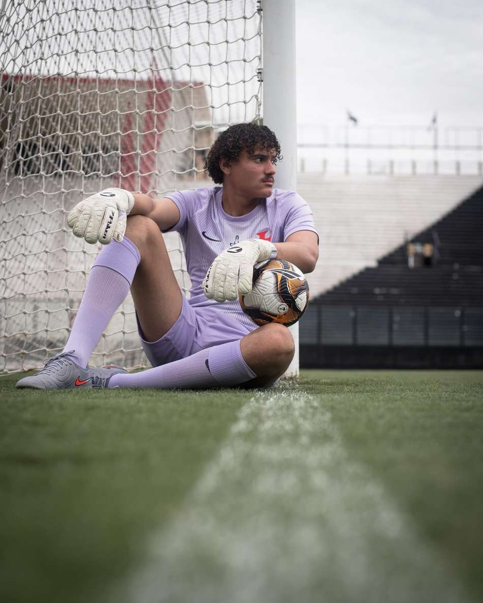 Philippe Gabriel, goleiro do Vasco, sentado no gramado junto à trave com a bola nos joelhos.