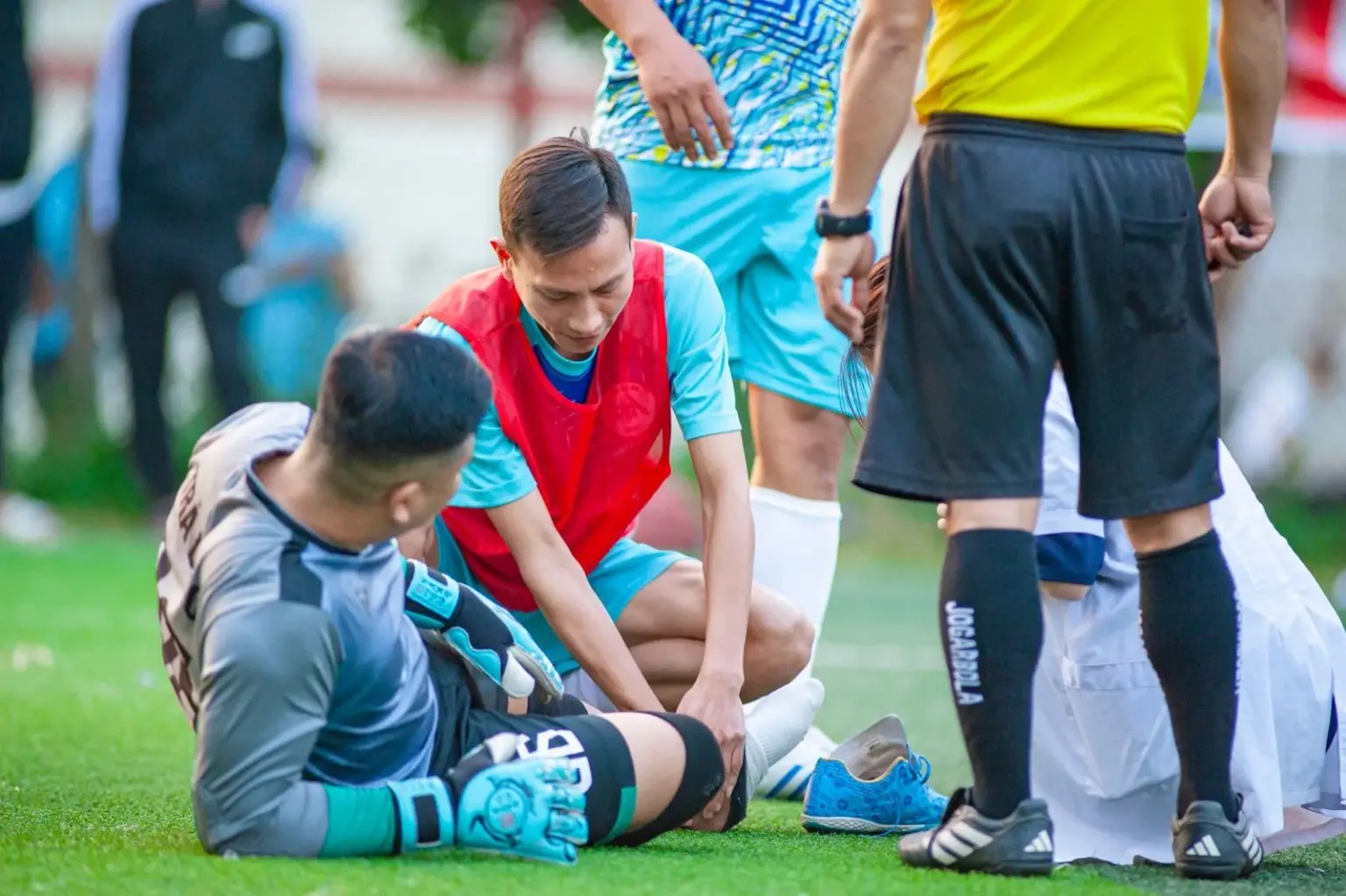 Injured footballer sitting on the pitch as a teammate checks on him during a match