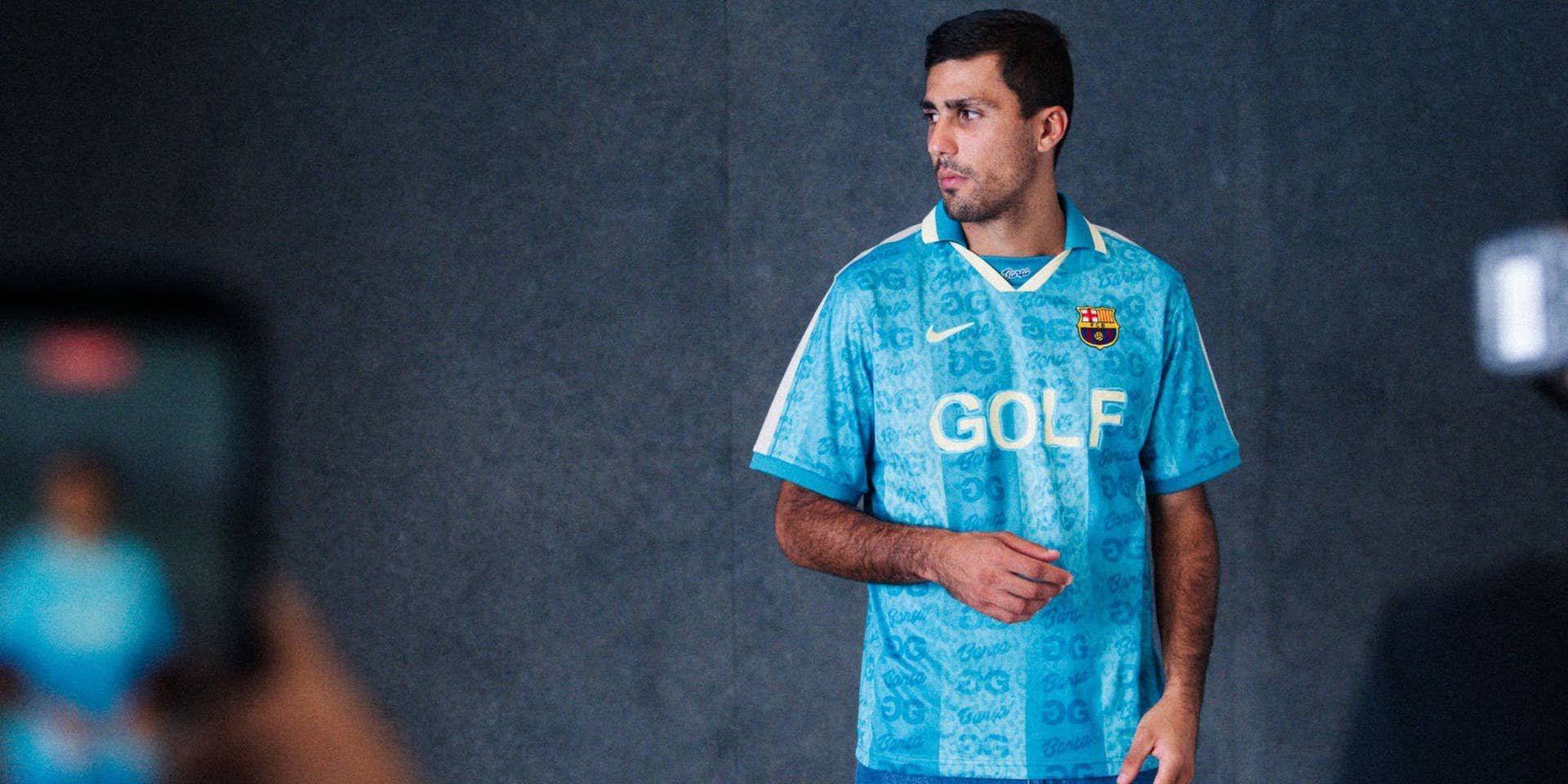 Ein Mann präsentiert das neue blaue Sondertrikot vom FC Barcelona vor dunklem Hintergrund.