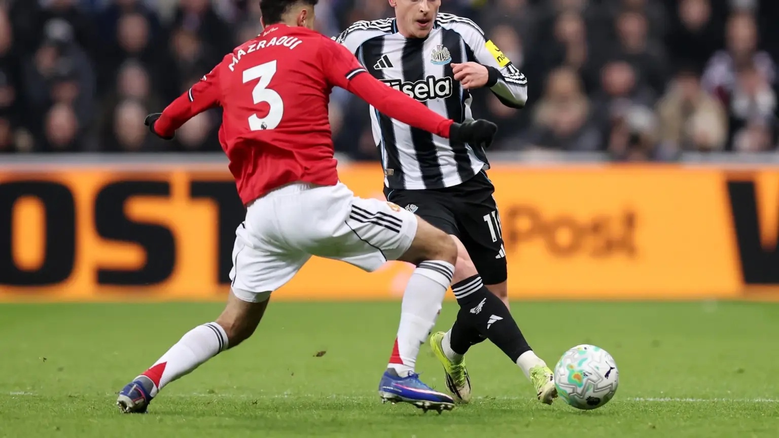 Noussair Mazraoui in a red Manchester United kit challenging a Newcastle United player for the ball.