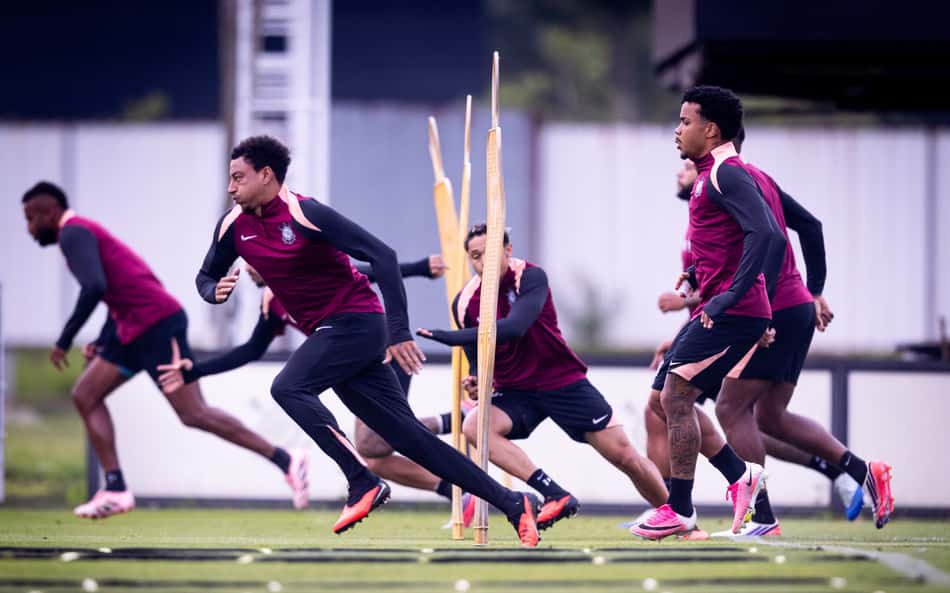 Grupo de jogadores de futebol treinando sprints entre postes de treino no campo.
