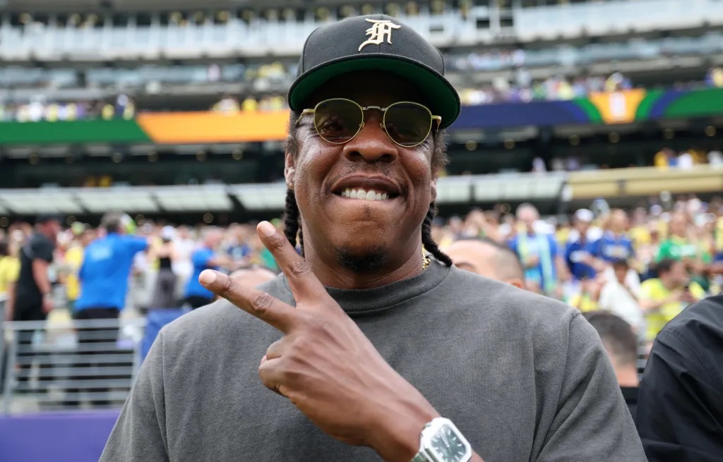 Jay-Z smiles and flashes a peace sign at a FIFA World Cup 2026 match.