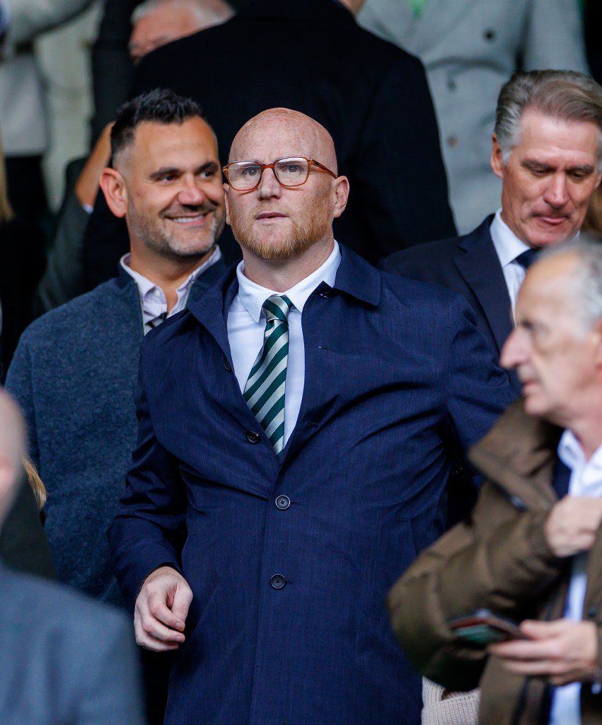 John Hartson wearing glasses, a white shirt, green and white striped tie, and a blue jacket.