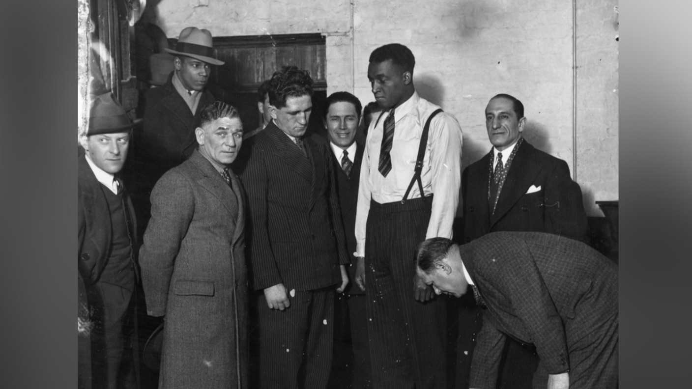 Johnson is being weighed on a scale in front of a number of men in suits looking at the scales.