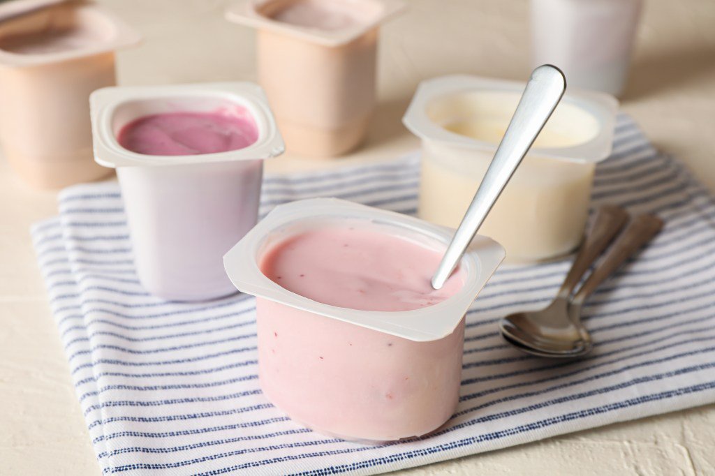 Plastic cups filled with yogurt and spoons on a white table.