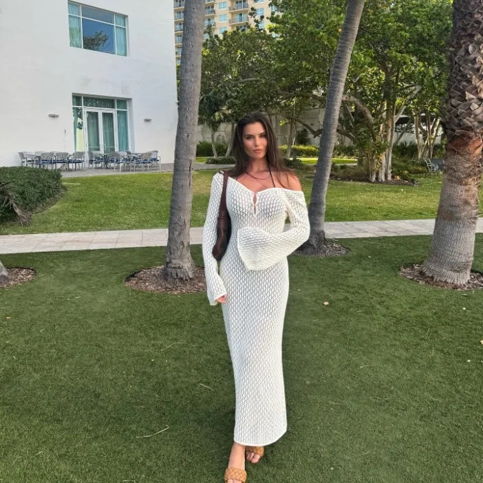 A woman in a white off-the-shoulder maxi dress with bell sleeves stands outdoors.