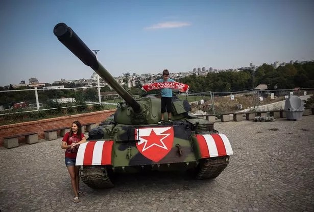 Red Star fans pose on a former Yugoslav army T-55 tank parked at the northern grandstand of the Rajko Mitic stadium in Belgrade