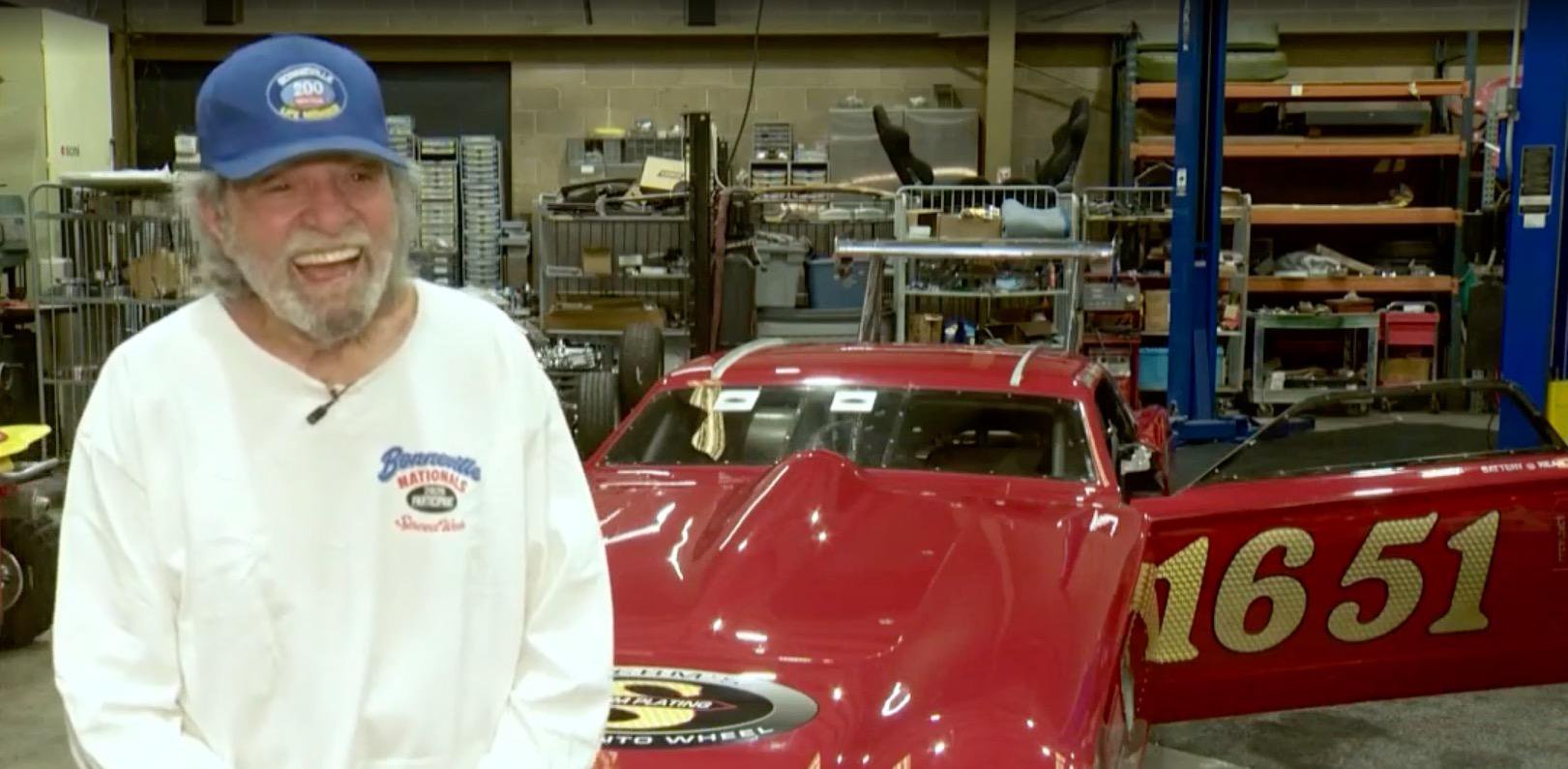 Gary Matranga smiling in front of a red race car in a garage.