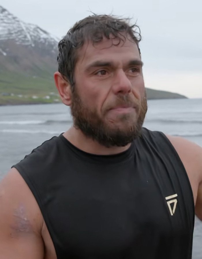 Extreme swimmer standing on a coastal shore near cold ocean waters looking tired after completing a swim challenge