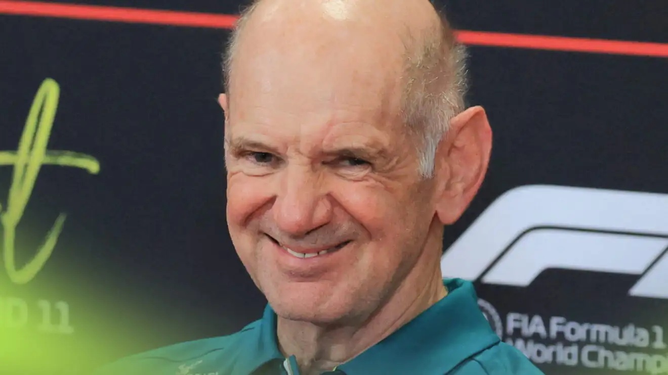 Adrian Newey grinning in a press conference while wearing a green Aston Martin shirt