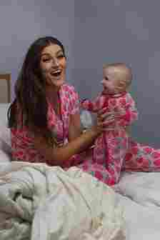 mum sits in bed holding baby and smiling