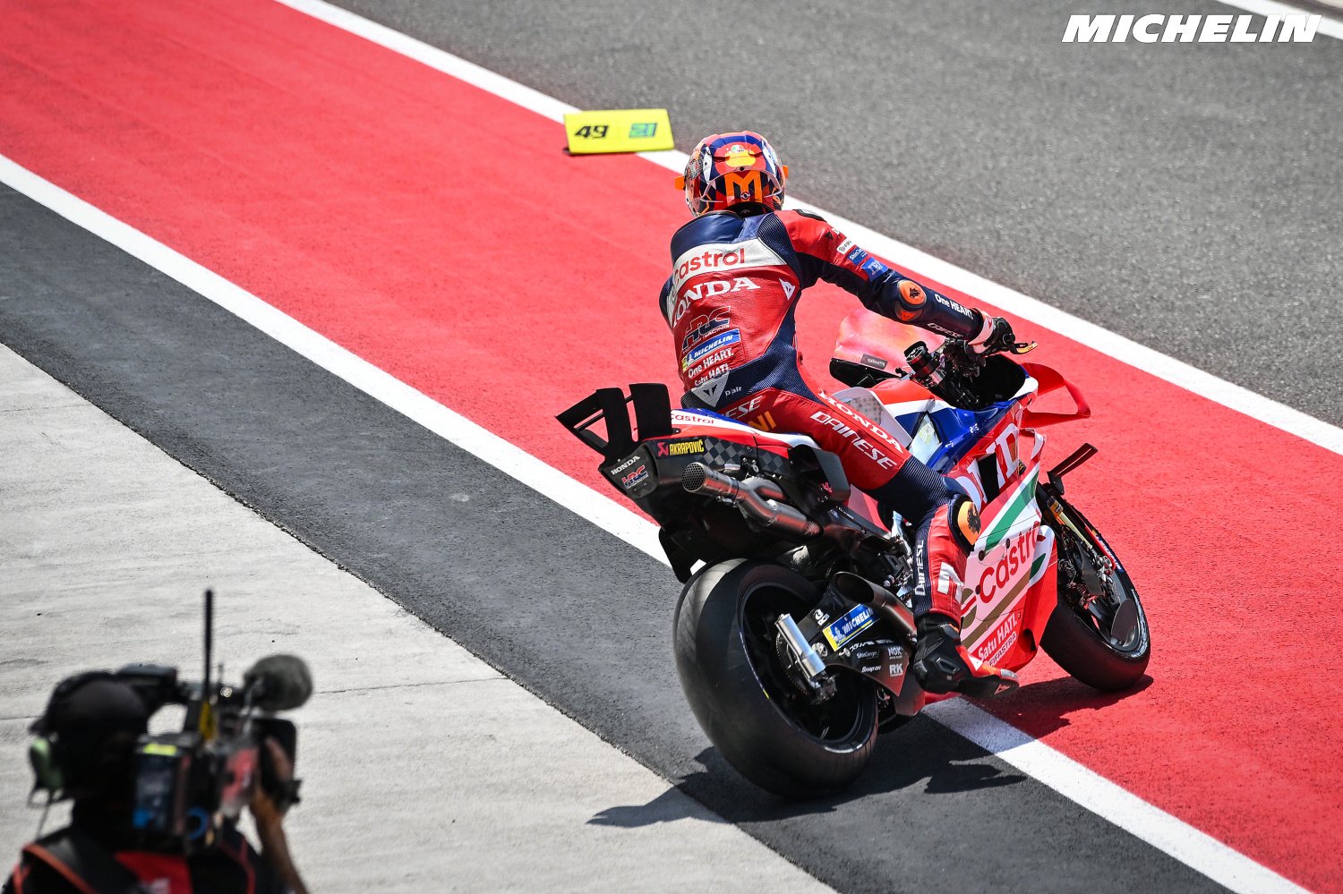 Honda MotoGP rider in red and navy leathers, with Castrol and Honda livery, riding back along the pit lane at Phillip Island