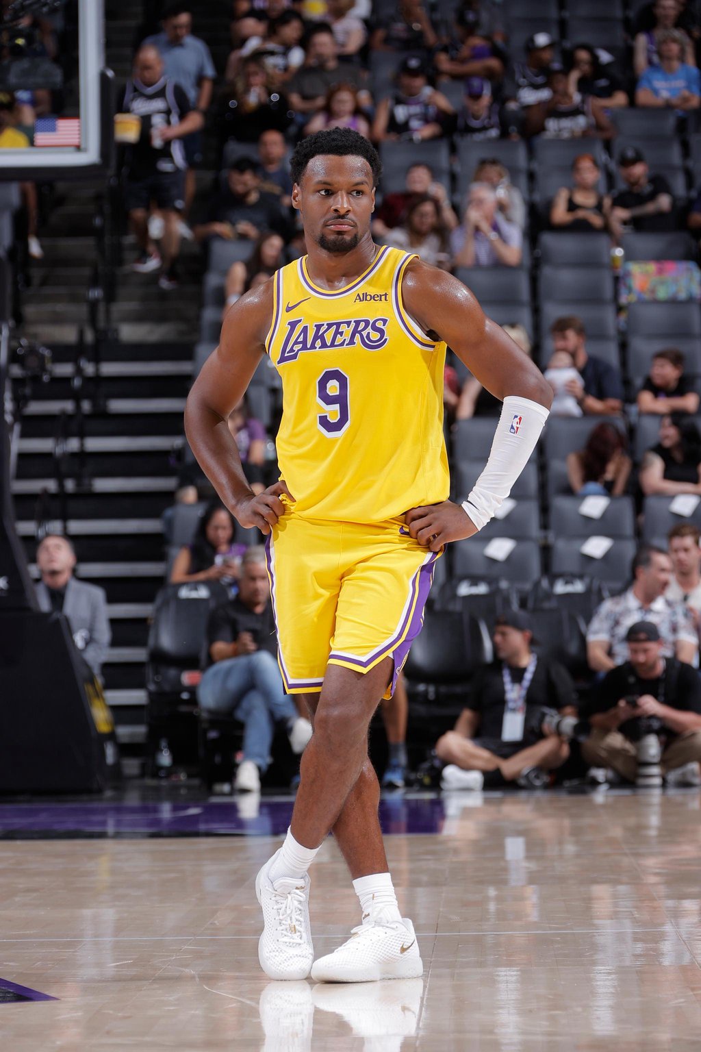 Los Angeles Lakers player Bronny James stands on the court with his legs crossed during a game against the Sacramento Kings.