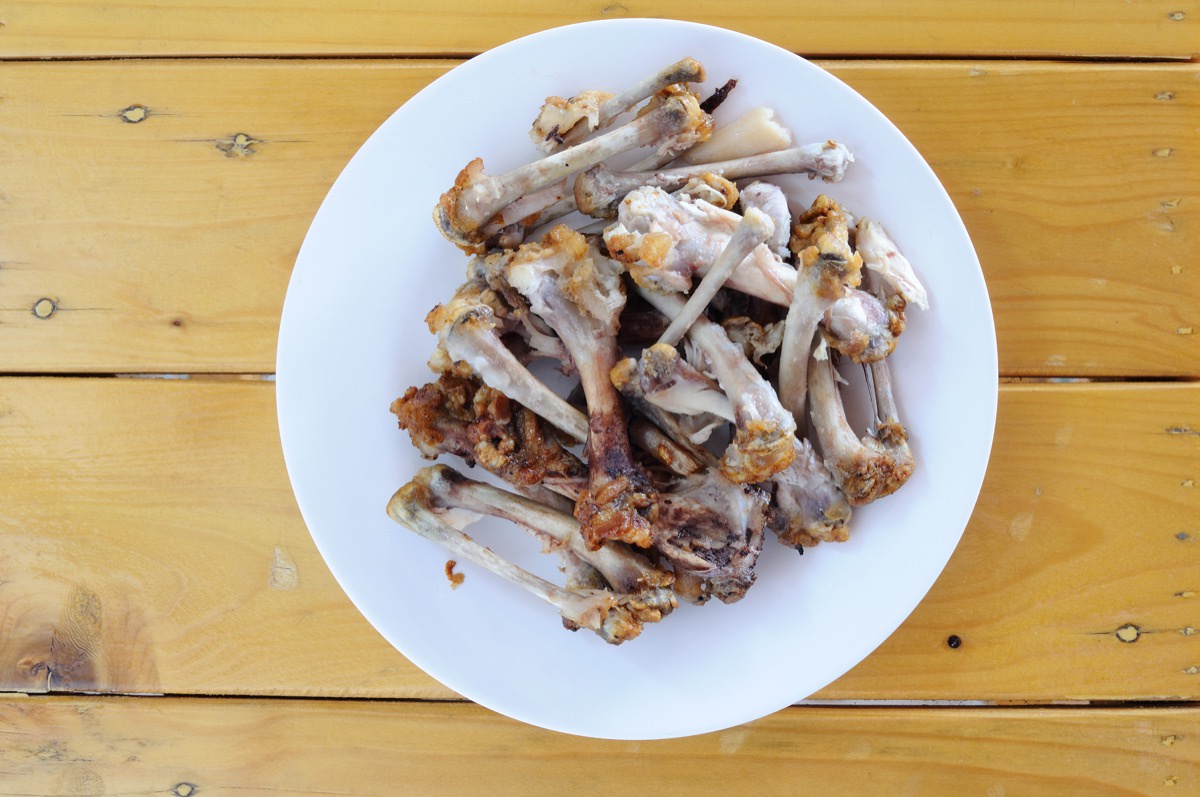 white plate on wooden table with chicken bones on it