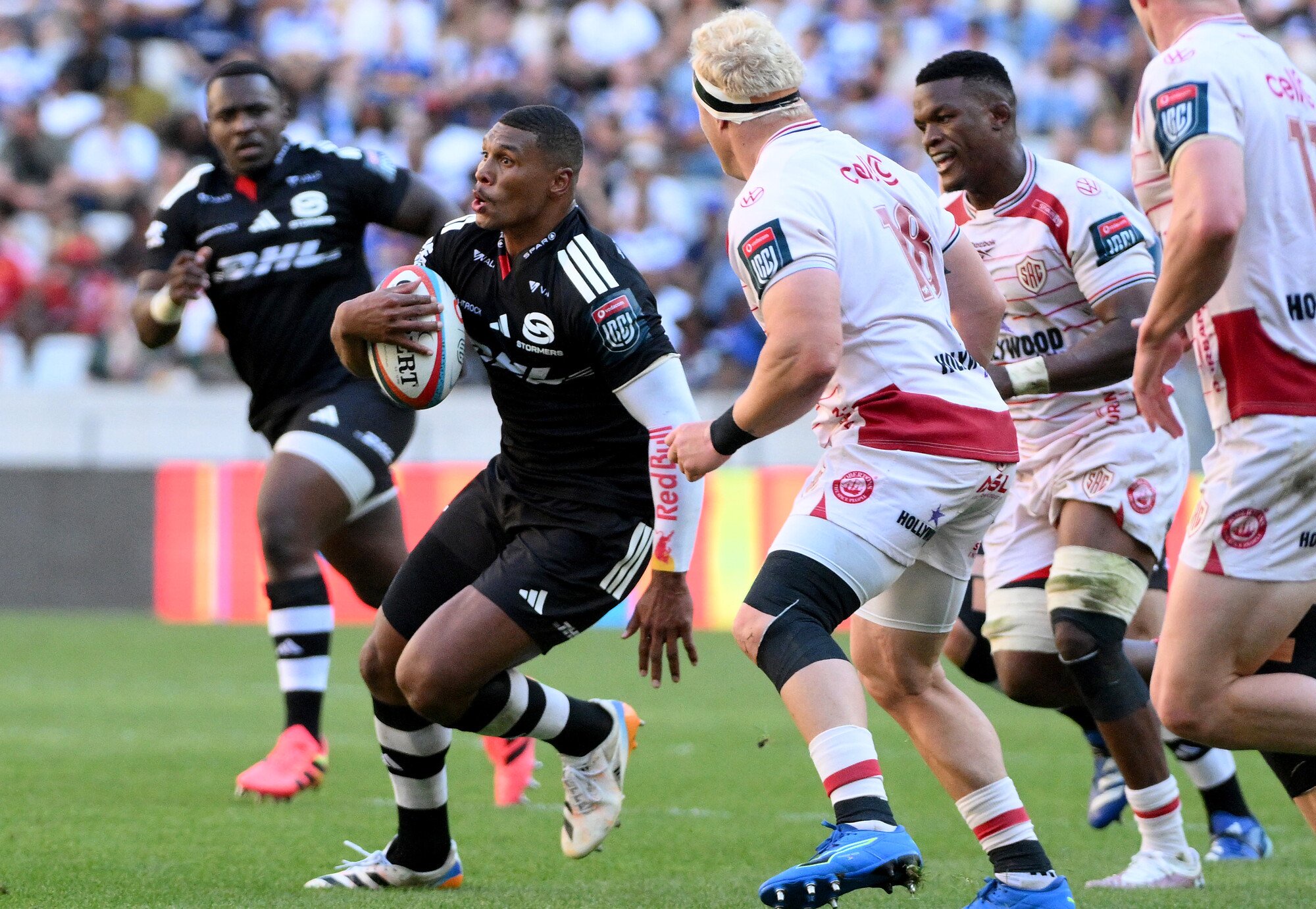 Rugby players in action on the field with one player holding a ball and another approaching.