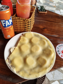 A plate sits on a wooden table holding a partially folded flatbread. Next to the plate is an orange Fanta can and a basket with condiments
