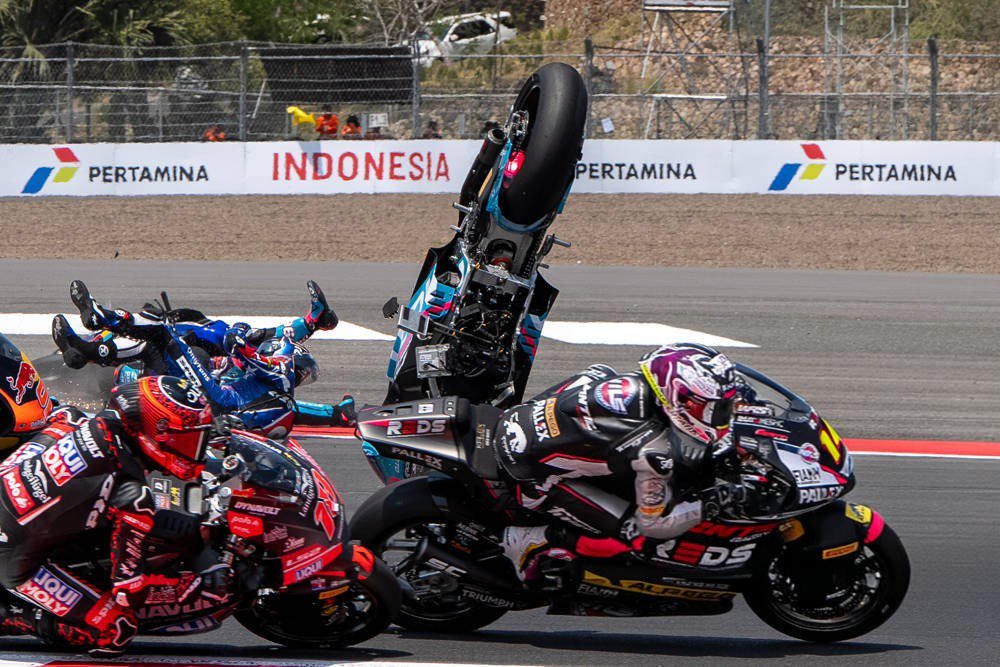 Motorcycle racers crash at Indonesia Moto2 race; one bike flips vertically while riders tumble past Pertamina banners on track