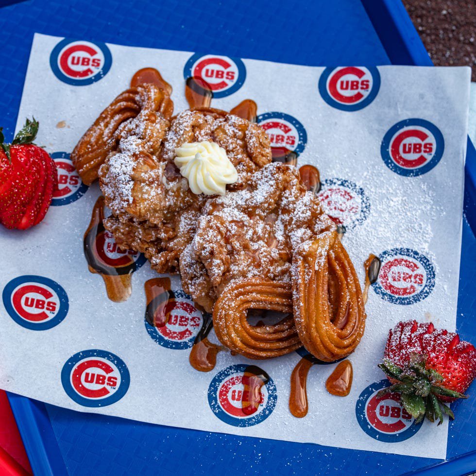 Churros topped with powdered sugar, whipped cream, and caramel sauce, served with strawberries.