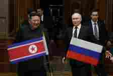 North Korea's leader Kim Jong Un, standing left, walks with Russian President Vladimir Putin, standing right. In the foreground, directly in front of both of them, are the North Korean and Russian flags, left and right, respectively.