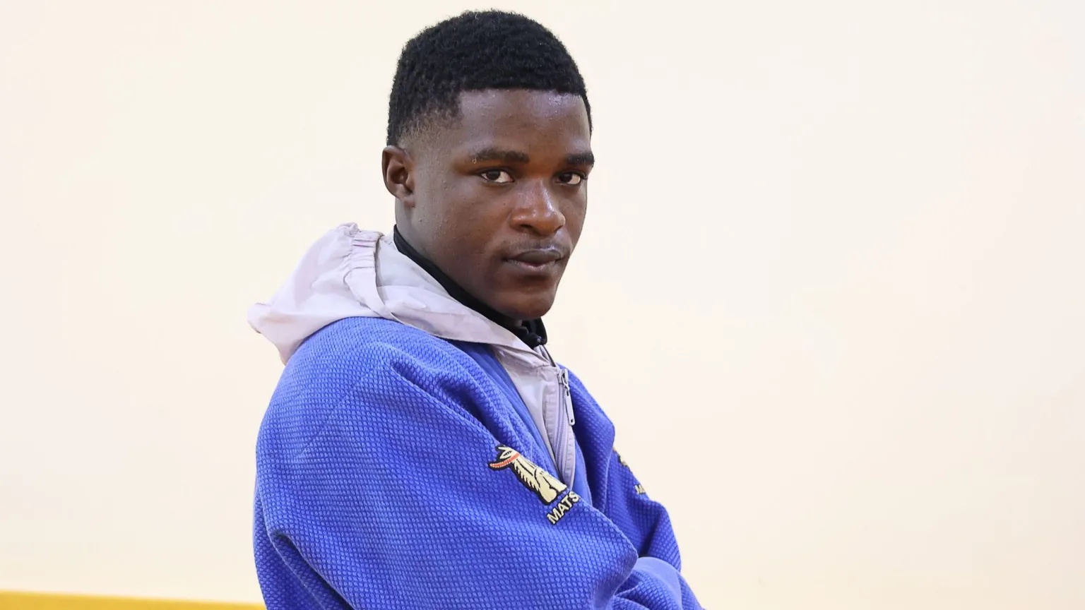 Getty Images Arno Yafunga Botay, visible from chest up wearing a light grey hoodie underneath a blue judo jacket, stands side on to the camera in front of a white wall and looks over his right shoulder into the lens with a determined expression
