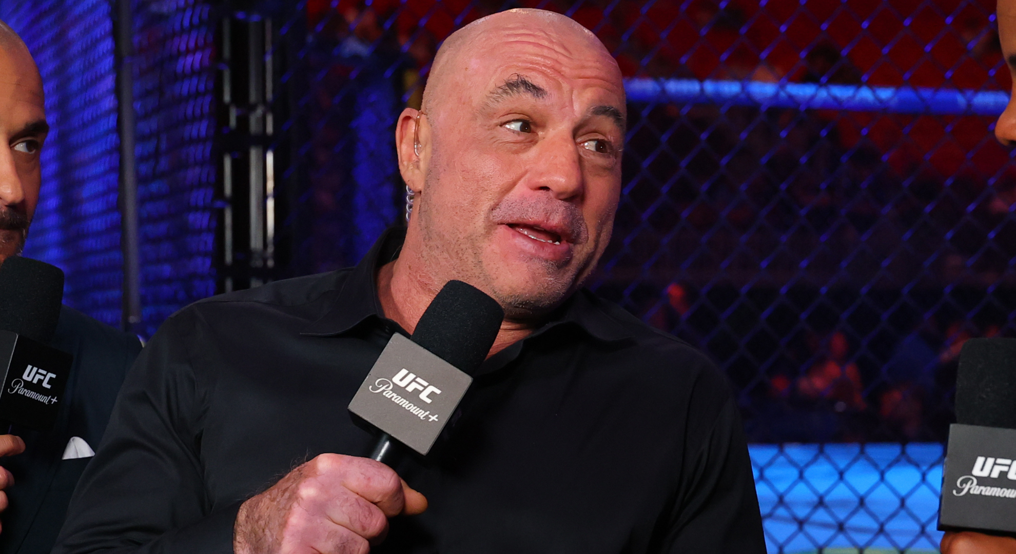 Joe Rogan speaks in an animated fashion into a 'UFC on Paramount+' microphone at cageside