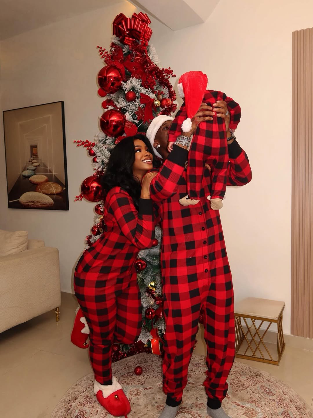 Priscilla Ojo and Juma Jux pose with their baby in matching red Christmas pyjamas beside a decorated Christmas tree