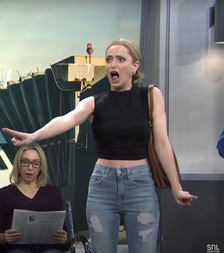 Sarah Sherman as a stressed traveler in a sleeveless crop top and ripped jeans gestures dramatically on a travel-themed set of SNL.