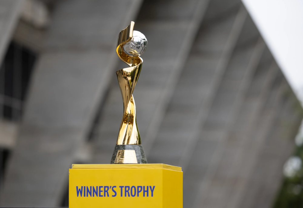 Taça dourada da Copa do Mundo Feminina da Fifa sobre pódio amarelo com a inscrição Winner's Trophy