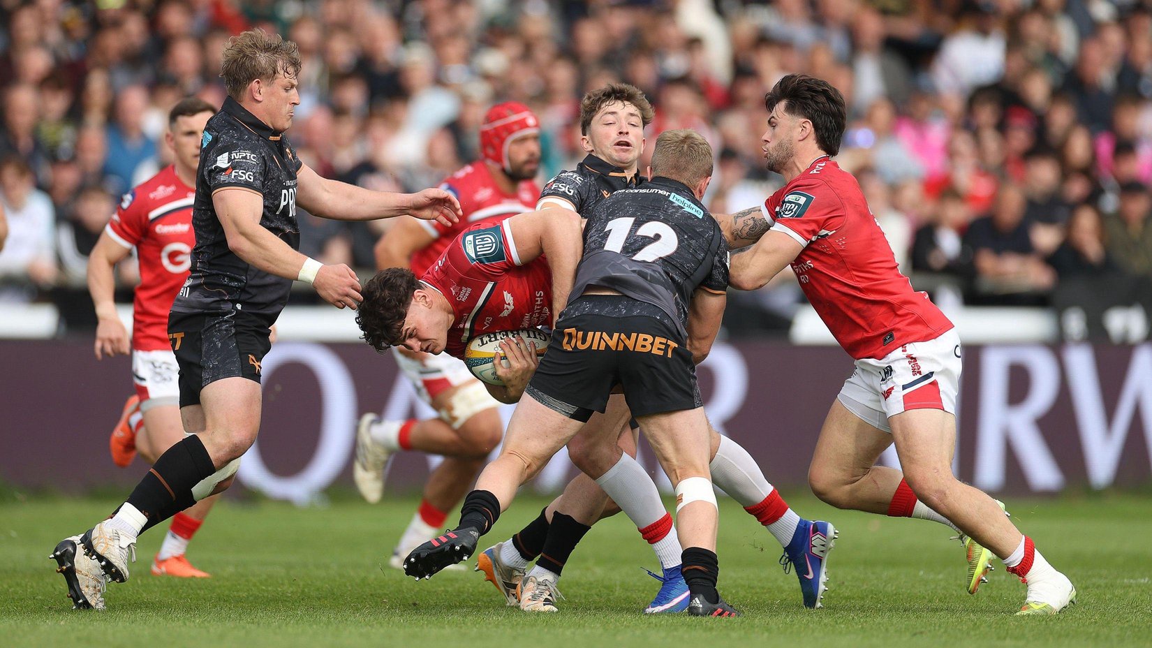 Ospreys players in black jerseys and shorts tackle Scarlets players in red jerseys and white shorts