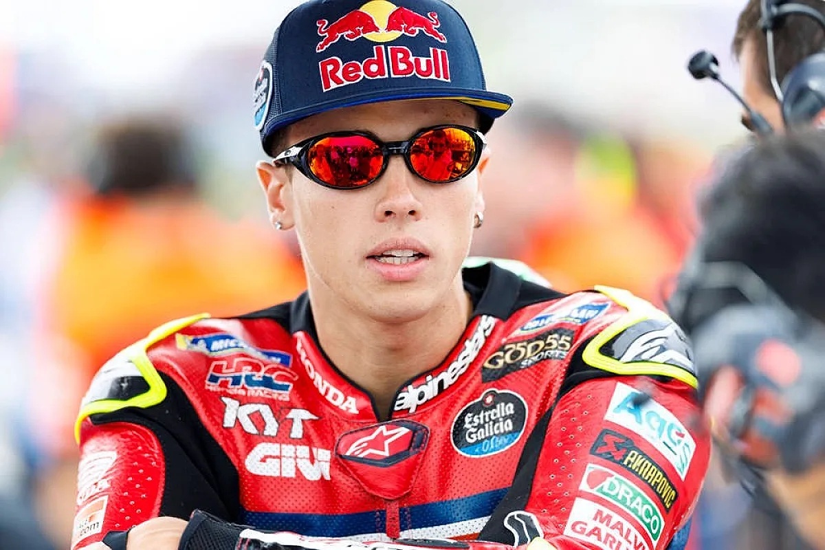 A rider in a red Honda leathers and Red Bull cap, with mirrored sunglasses, in the MotoGP paddock. Sponsors include HRC, KTM and Estrella Galicia.