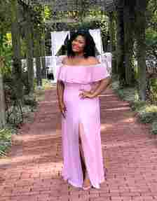 a reviewer in an off-shoulder ruffled pink gown with a leg slit, posing outdoors