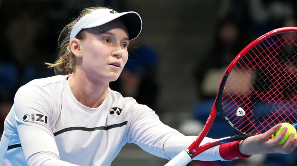 Elena Rybakina prepares to serve the ball in Tokyo, holding a red and black tennis racquet and wearing a white tennis outfit