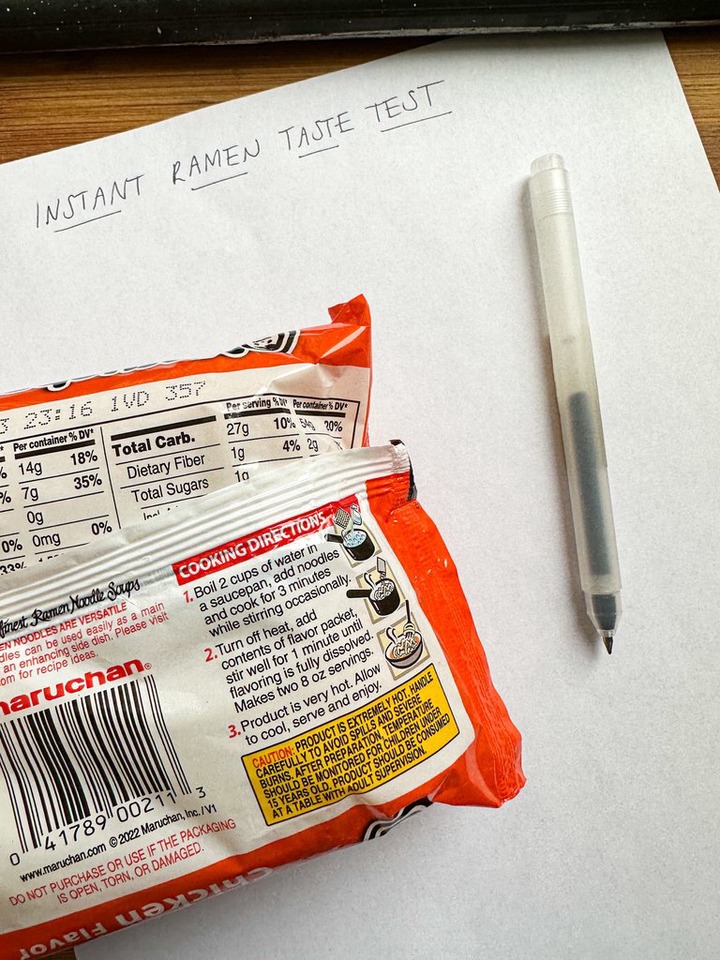 packet of ramen, instant ramen taste test written on paper, with pen on top